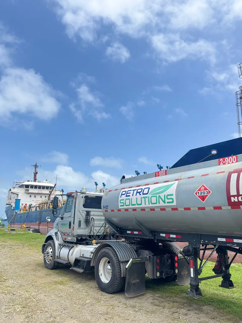 PetroSolutions tank truck parked on grass next to a docked tanker ship under a blue sky