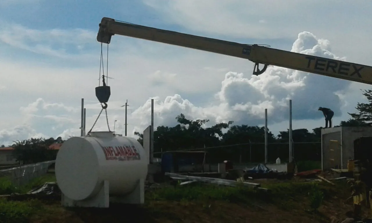 Grúa izando un tanque de combustible con la leyenda «Inflamable» en un terreno en construcción