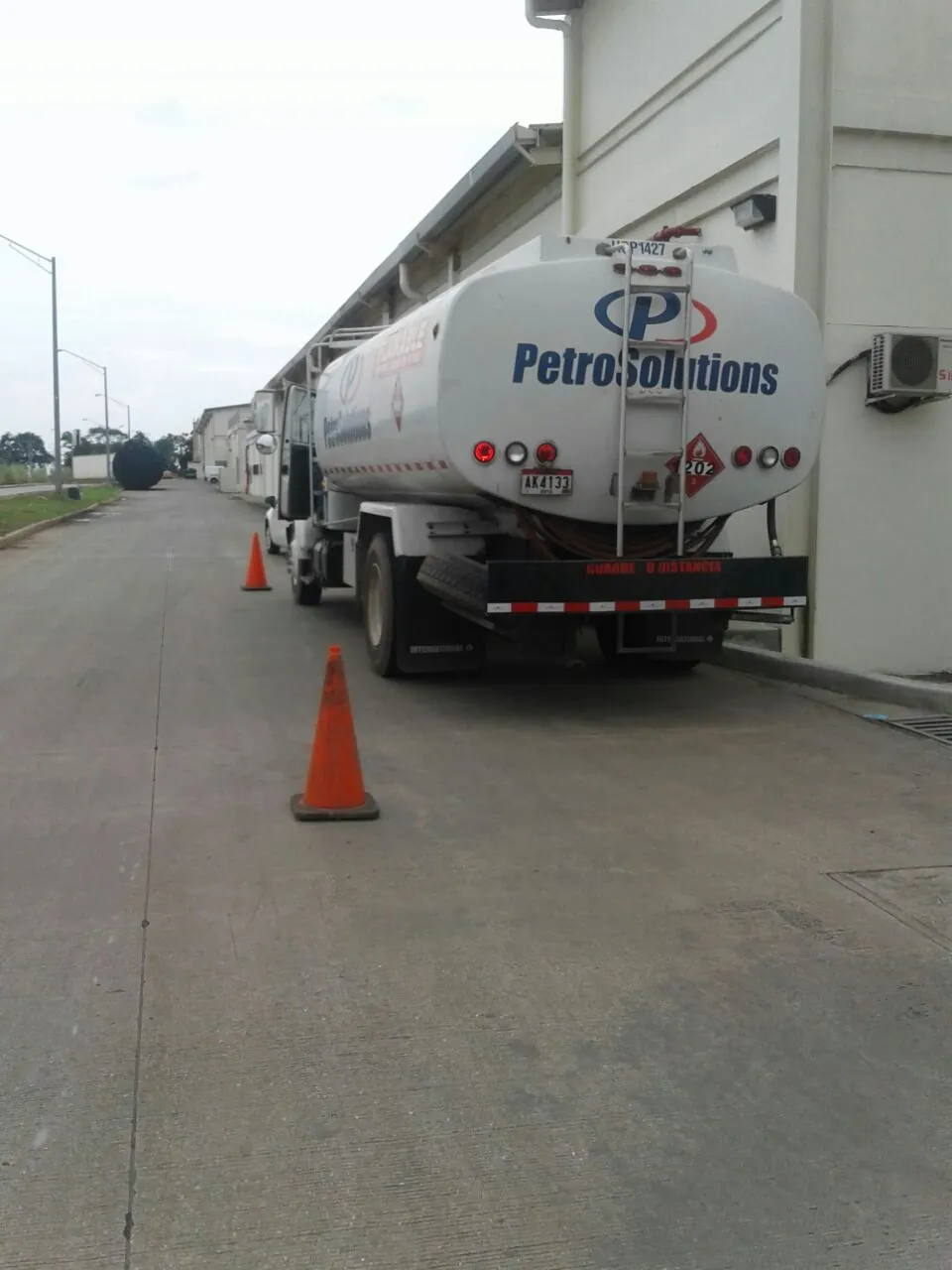 Parte trasera de un camión cisterna de PetroSolutions estacionado junto a una nave industrial, con conos de seguridad