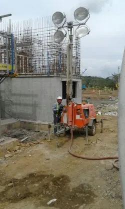 Trabajador con casco junto a una torre de iluminación portátil en una obra