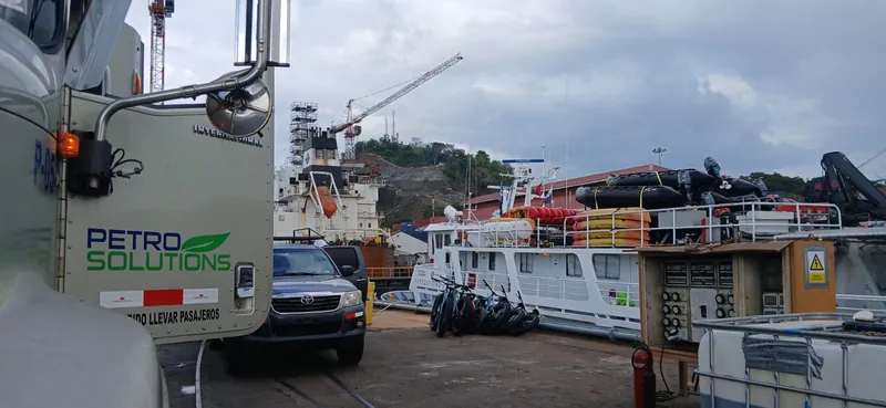 PetroSolutions truck at a shipyard next to a white vessel loaded with inflatable boats, with cranes behind