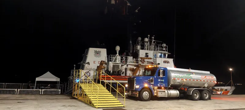 PetroSolutions tank truck on a pier at night beside a docked vessel and its boarding stairs